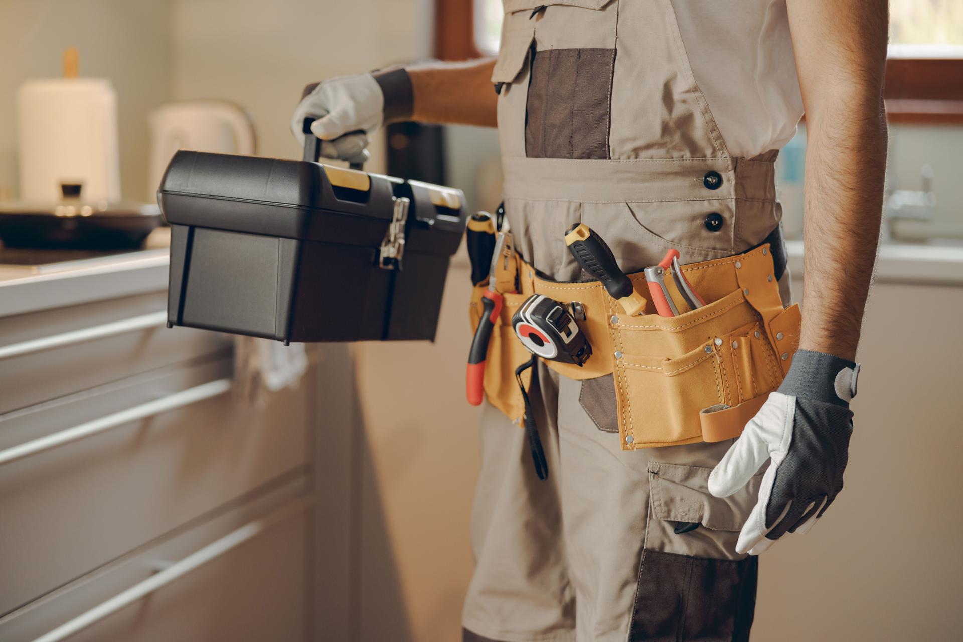 Close up do reparador de uniforme em pé na cozinha de casa e segurando sua bolsa de ferramentas